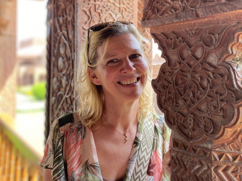 Sylvia glimlacht, met een houtsnijwerk op de achtergrond