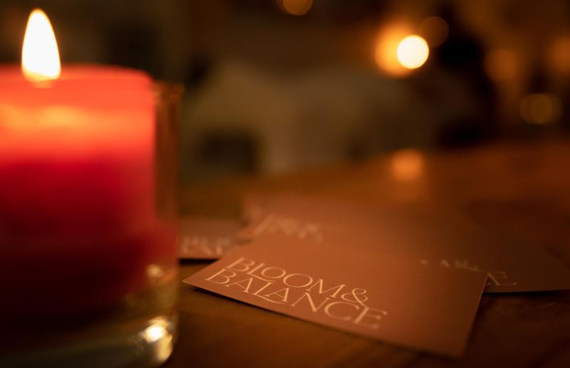 Een brandende kaars naast kaartjes van Bloom &amp; Balance op een houten tafel
