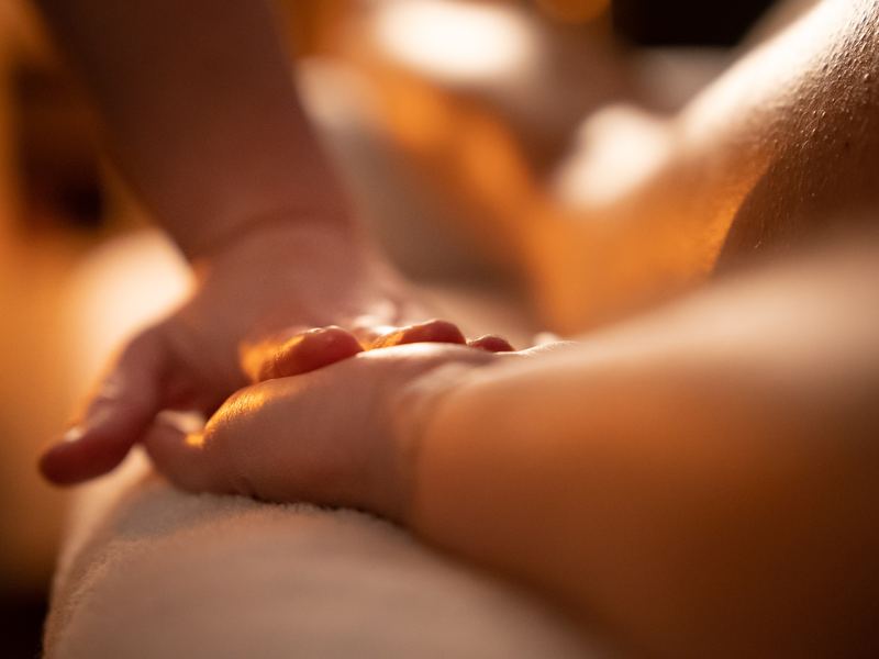 Een hand rust zacht op een rug, in warm kaarslicht