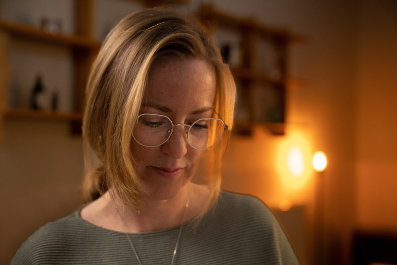 Lesley kijkt glimlachend naar beneden in haar praktijkruimte bij kaarslicht