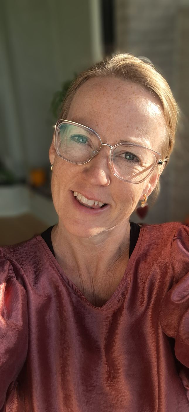 Lesley in een oudroze bloes, lachend naar de camera