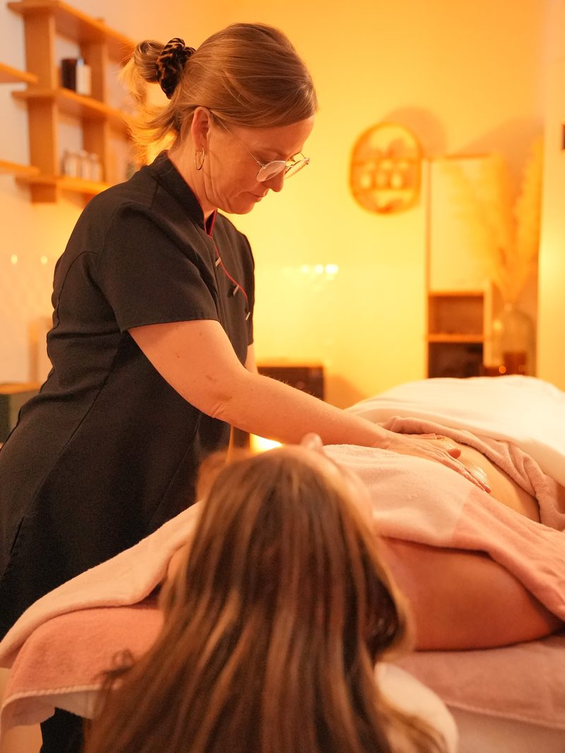 Lesley masseert aandachtig de rug van een cliënte die onder roze handdoeken op de massagetafel ligt